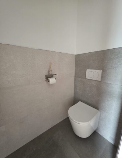 Toilettes rénovées avec WC suspendu, carrelage gris et finitions minimalistes.