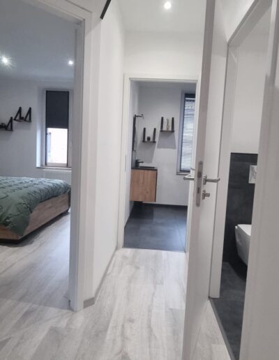 Couloir rénové avec sol clair, murs blancs et accès vers chambre et salle de bain moderne.