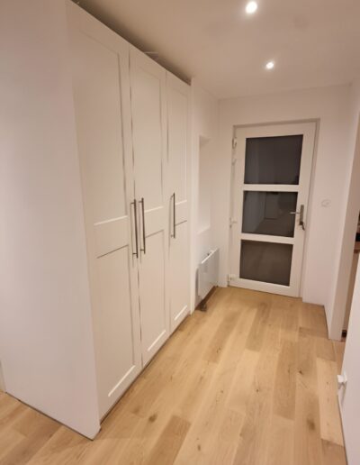Entrée intérieure avec placards blancs intégrés, parquet en bois et éclairage encastré moderne