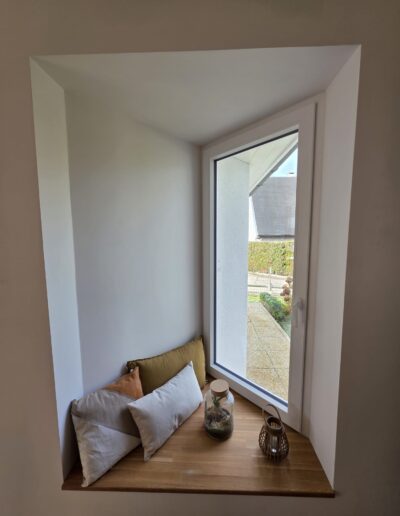 Espace aménagé près d’une fenêtre avec assises, coussins et vue sur l’extérieur lumineux
