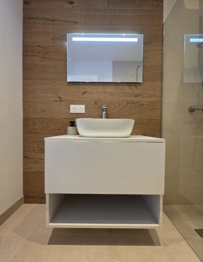 Salle de bain rénovée avec meuble blanc suspendu, vasque moderne et mur en bois décoratif.