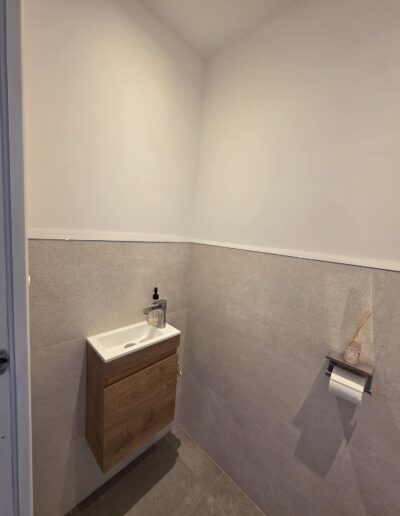 Toilettes rénovées avec meuble suspendu en bois, petite vasque et murs aux finitions modernes.