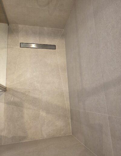 Douche à l’italienne rénovée avec carrelage beige grand format et évacuation linéaire intégrée.