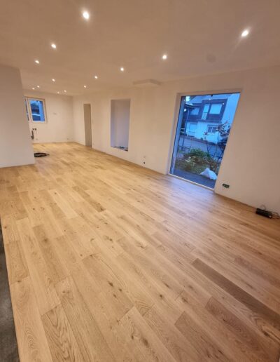 Grande pièce de vie rénovée avec parquet en bois, spots encastrés et ouverture vers l’extérieur.