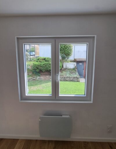 Fenêtre rénovée avec cadre blanc, vue sur le jardin et mur aux finitions propres.